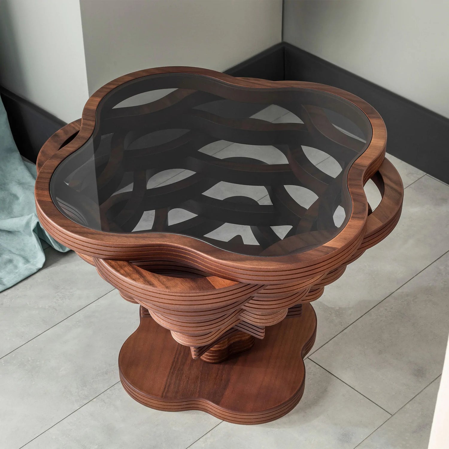 A cloud-shaped coffee table with a wooden structure and a glass top, featuring built-in handles and placed on a tiled floor.