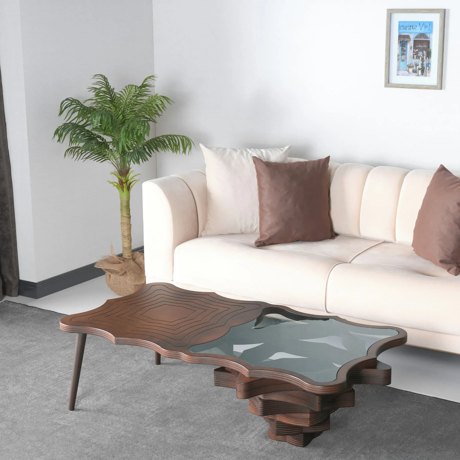 A stylish coffee table with a unique layered design, featuring wood and glass elements, placed in a living room setting with a white sofa and decorative pillows.