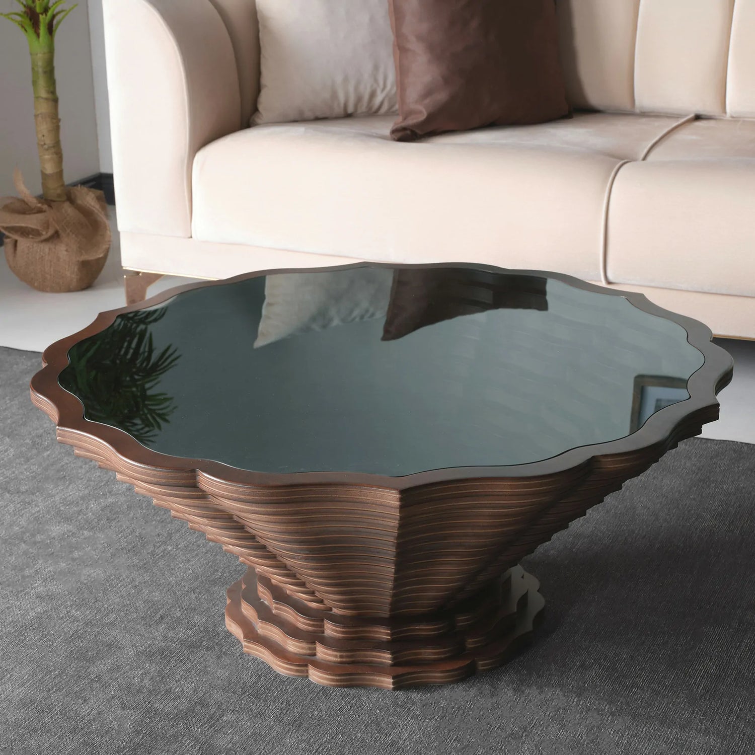 A round wooden side table with a scalloped edge design and a dark glass top, placed on a white floor.