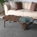 A star-shaped coffee table with a wood edge and glass top, placed in a room with a beige sofa and decorative pillows.