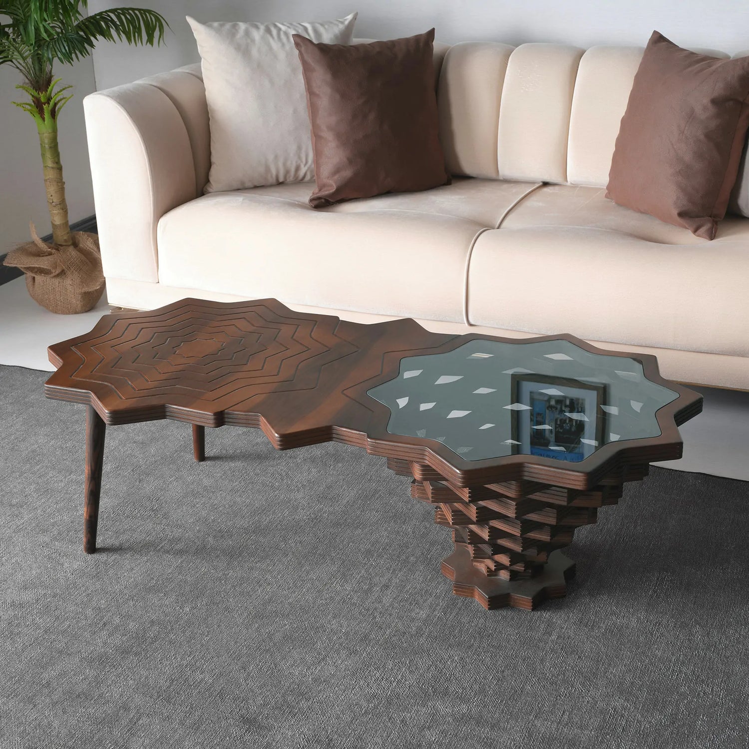 A star-shaped coffee table with a wood edge and glass top, placed in a room with a beige sofa and decorative pillows.